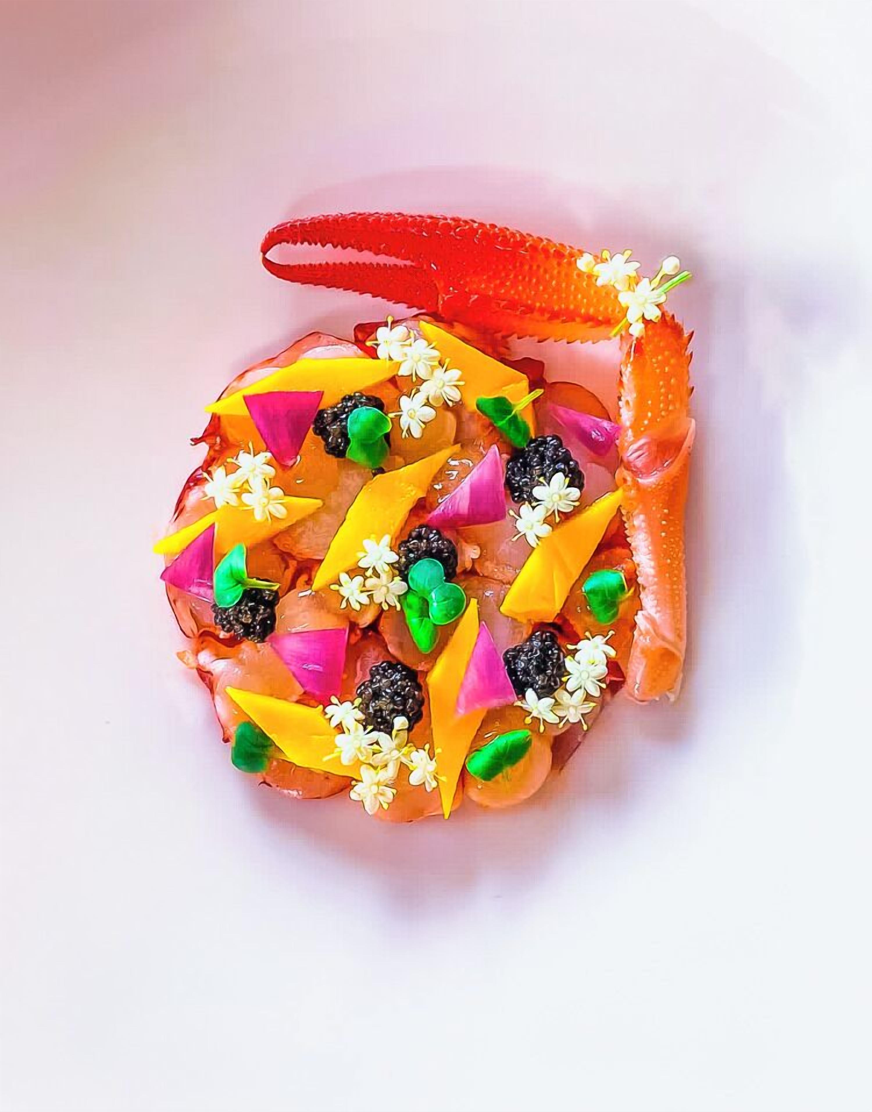 A dish with a crab leg, colorful vegetables, and flowers.