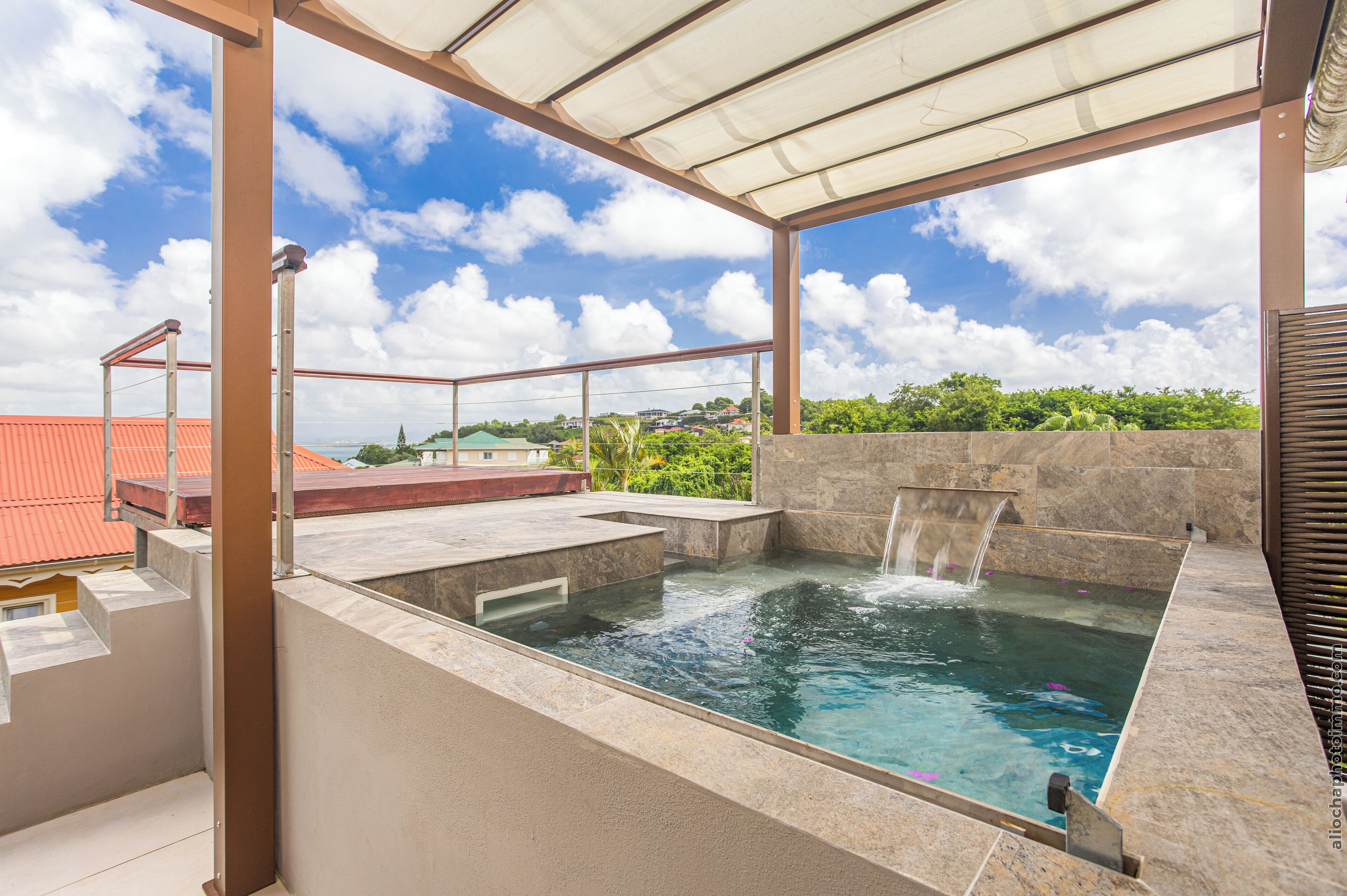 A rooftop pool with a waterfall feature, surrounded by a covered area with a view of the cityscape.