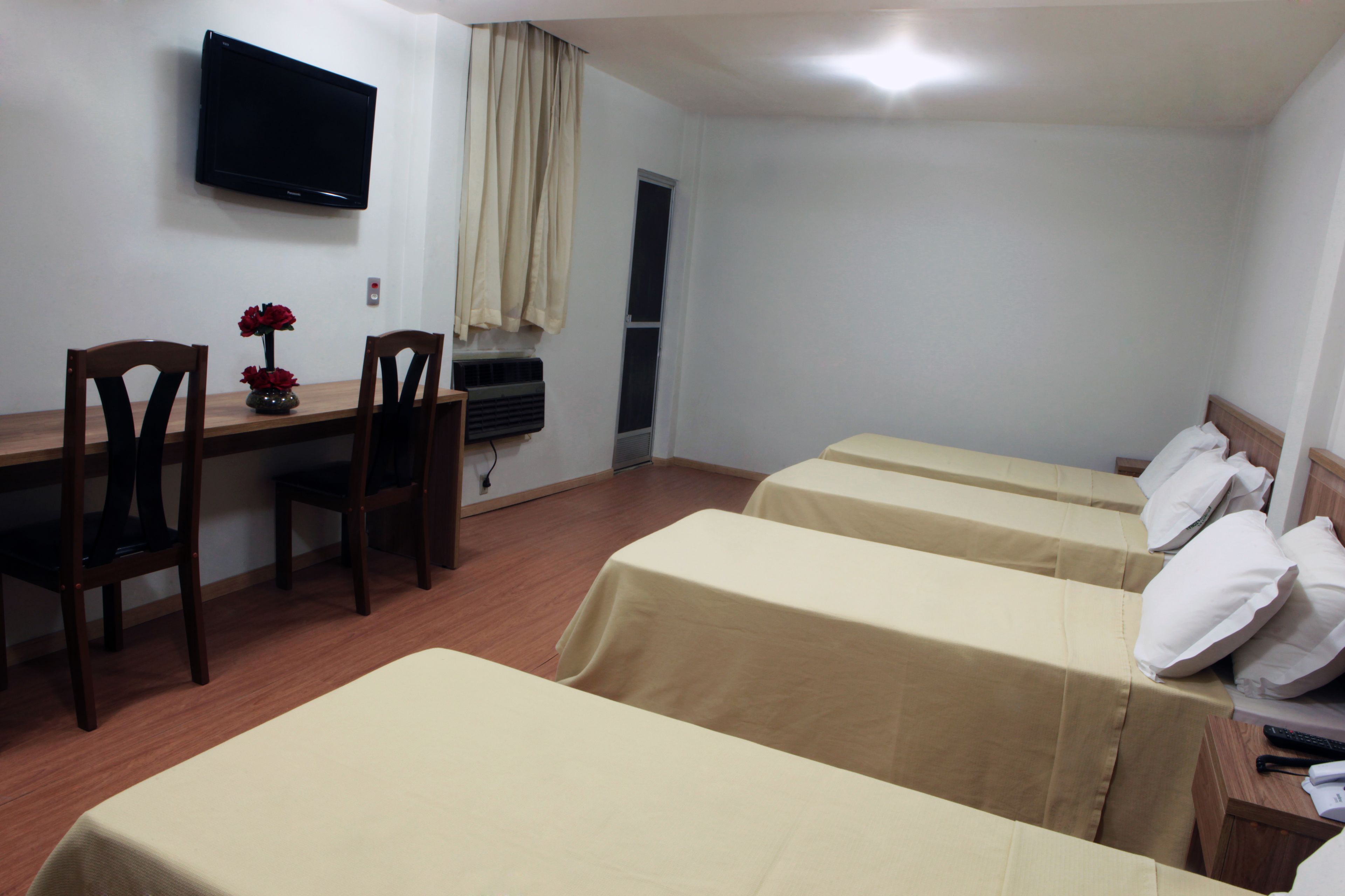 A hotel room with a desk, two beds, a TV, and a window with curtains.
