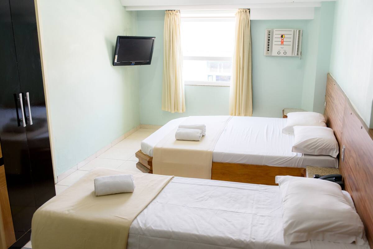 Habitació d'hotel amb dos llits, televisió, termòstat i finestra amb cortines.