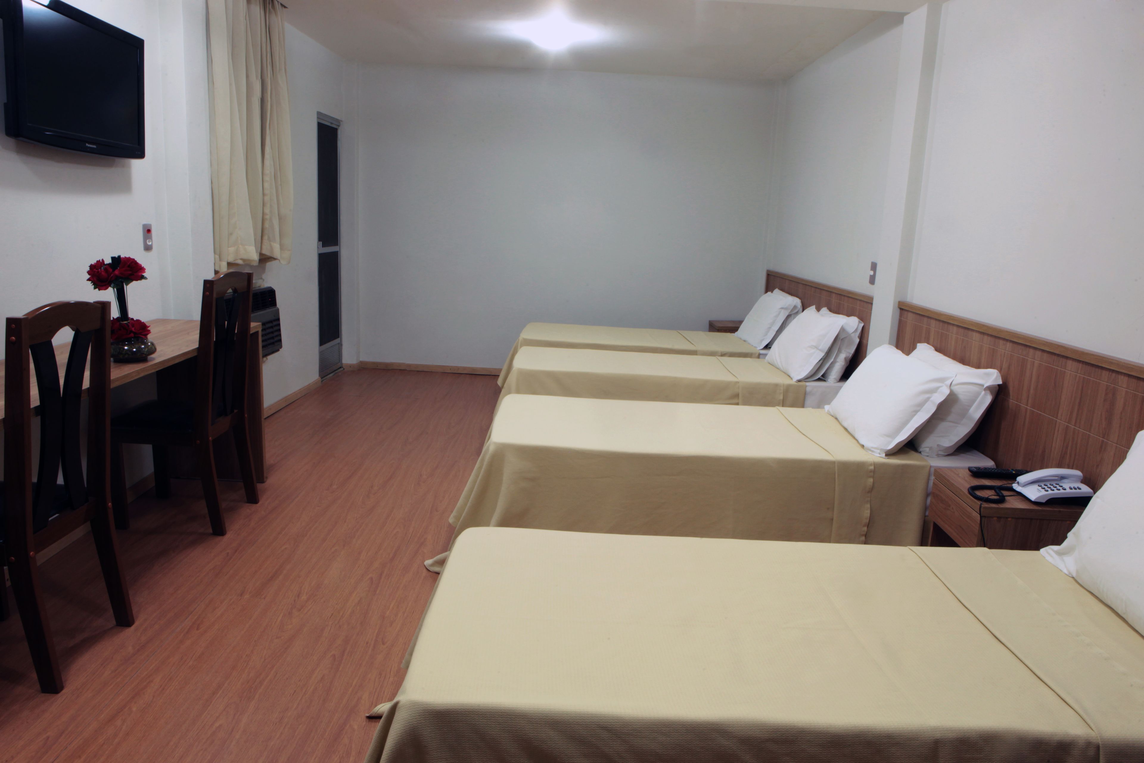 A hotel room with three beds, a desk with a chair, a TV mounted on the wall, and a door.