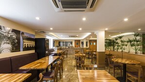 Un restaurante con mesas y sillas de madera, una zona de bar y un espacio de estar con un sofá.