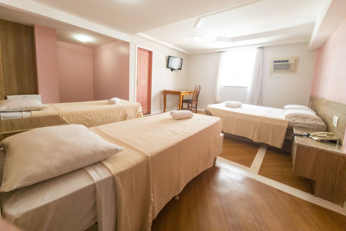 Habitació d'hotel amb tres llits individuals, un escriptori de fusta, una cadira, un televisor i un telèfon.