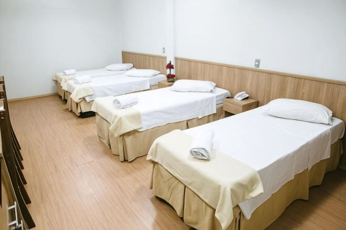 A hotel room with four single beds, wooden flooring, a bedside table with a lamp, and a telephone.