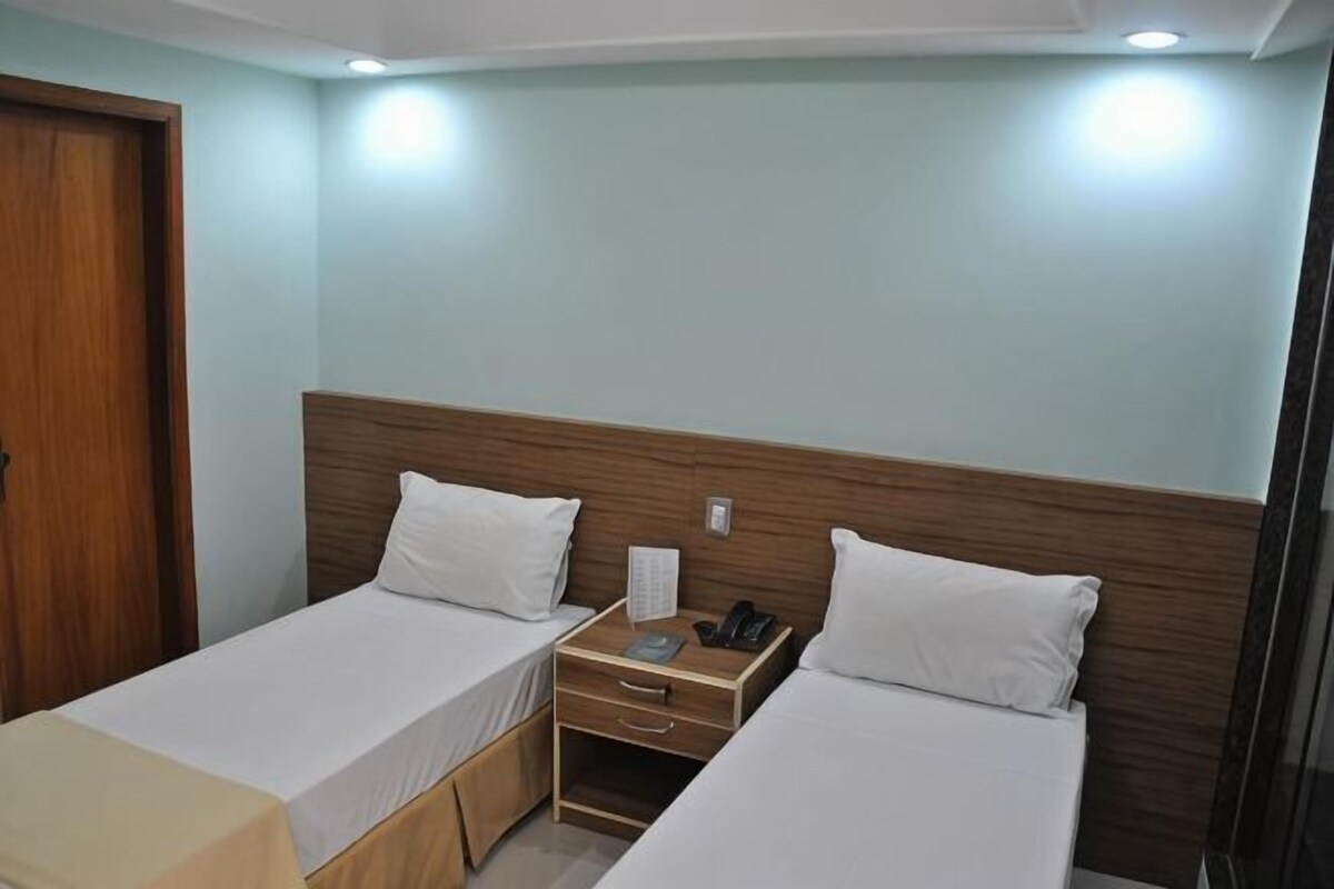 A hotel room with two single beds, a wooden headboard, a bedside table with a phone and a lamp, and a door.