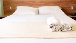 Una cama bien hecha con sábanas blancas y dos toallas enrolladas sobre un edredón color beige.