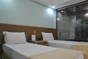 A hotel room with two beds, a wooden headboard, a bedside table with a phone, and a glass partition. - Gamboa Rio Hotel (Rio de Janeiro)