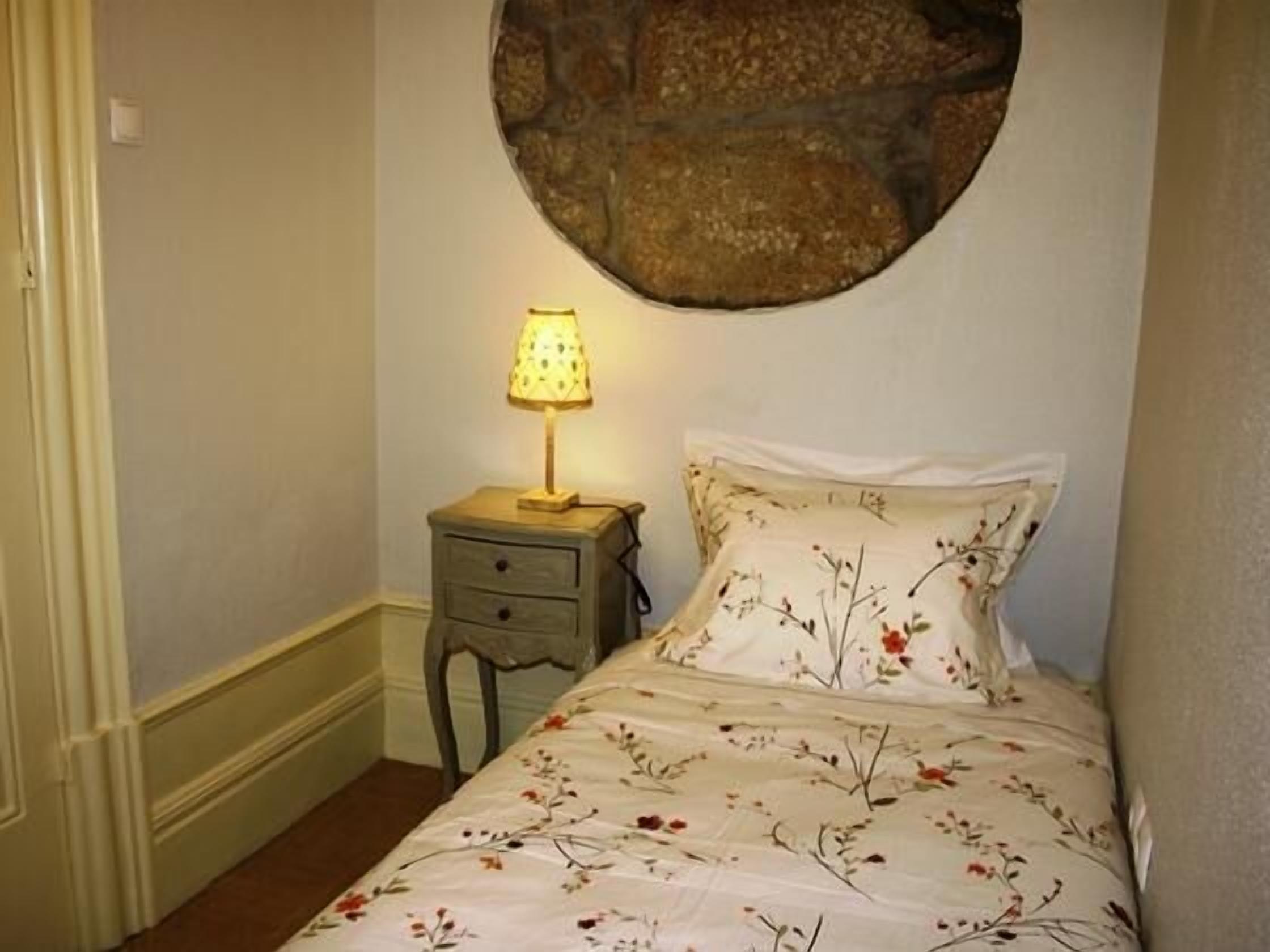 A bedroom with a bed, a nightstand with a lamp, and a stone wall.