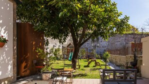 Une terrasse avec des meubles d’extérieur, un mur en pierre et une zone herbeuse avec un arbre.