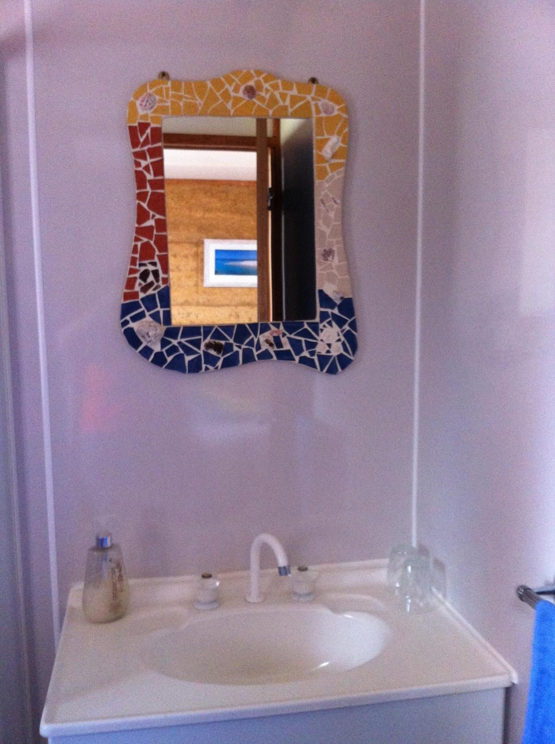 A bathroom with a mosaic-patterned mirror, a white sink, and a small bottle on the counter.