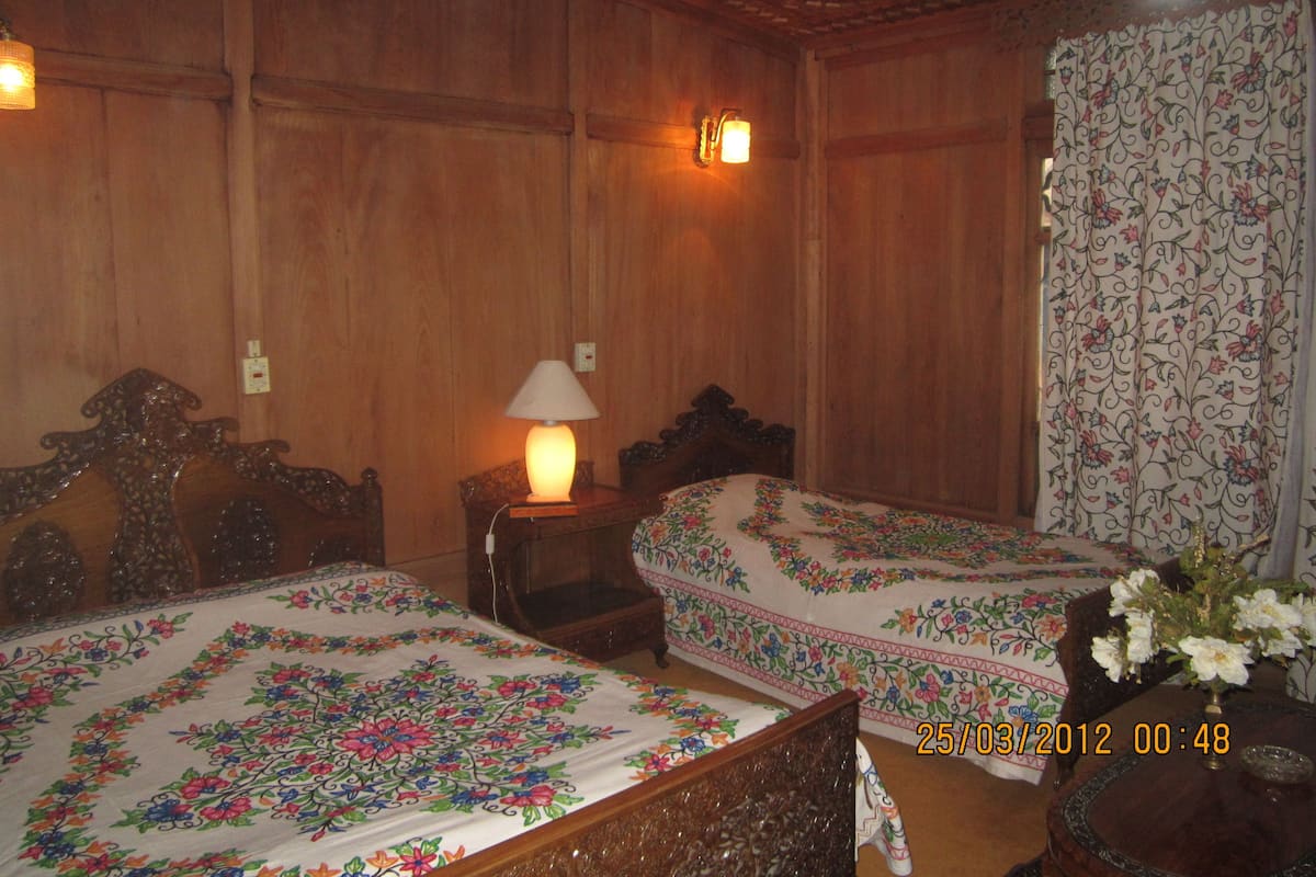 Quarto com duas camas de madeira, uma mesa de cabeceira com abajur e cortina florida.