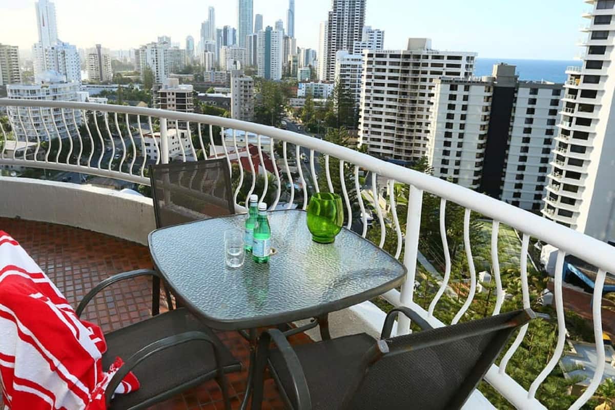 A balcony with a table and chairs, a red and white towel, and a view of a cityscape with tall buildings.