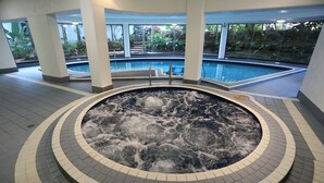 A hot tub area with a view of an outdoor pool and surrounding greenery.