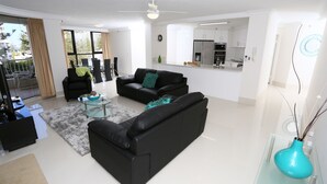 A modern living room with a black sofa, a glass coffee table, and a teal vase.