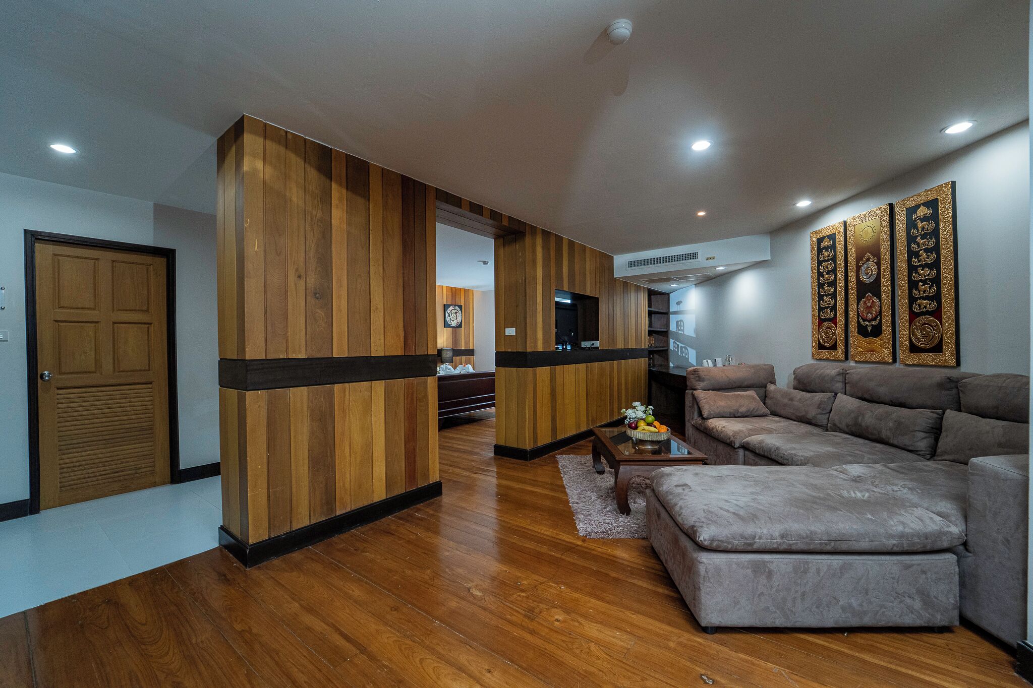 Una sala de estar moderna con una pared de acento de madera, un sofá seccional gris y una pequeña mesa de centro con fruta.