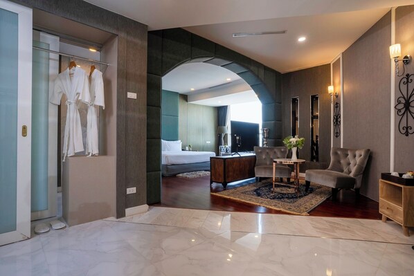 Ein modernes Hotelzimmer mit Marmorboden, einem Bett, einer Sitzecke mit Tisch und Stühlen sowie einem Badezimmer mit Dusche und Handtuchhalter.