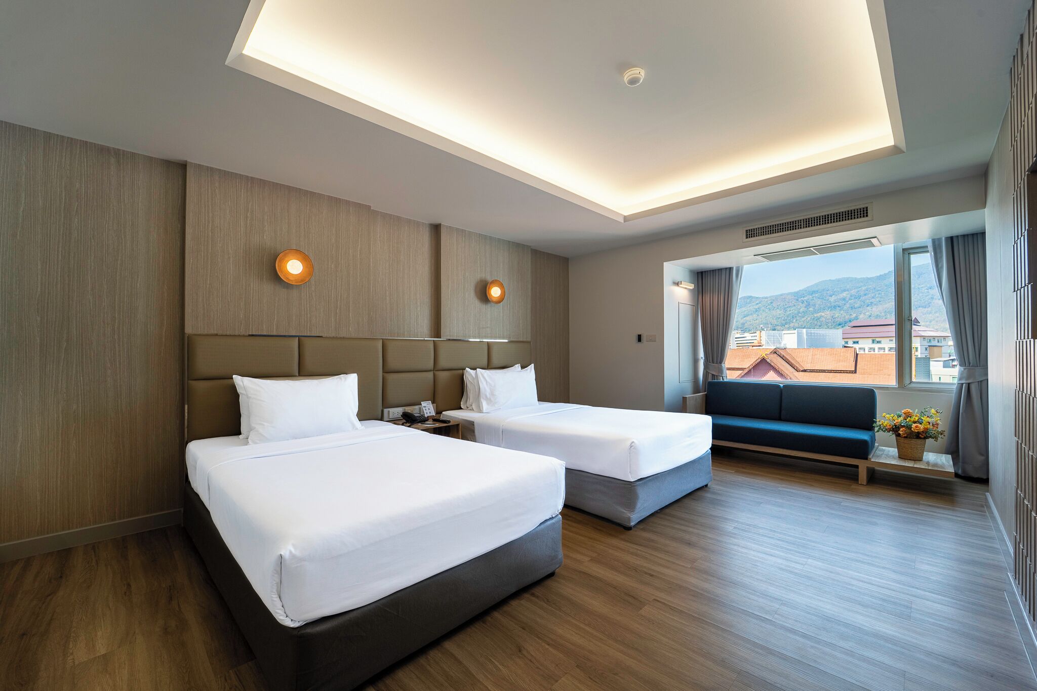 A hotel room with two beds, a sofa, a window with a view, and a ceiling light.
