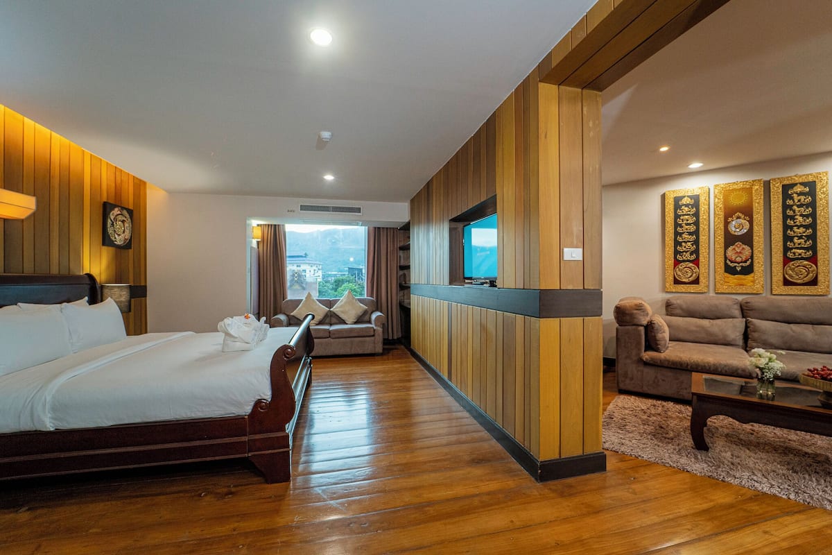 Een hotelkamer met houten vloer, een bed, een bank, een televisie en decoratieve wandpanelen.