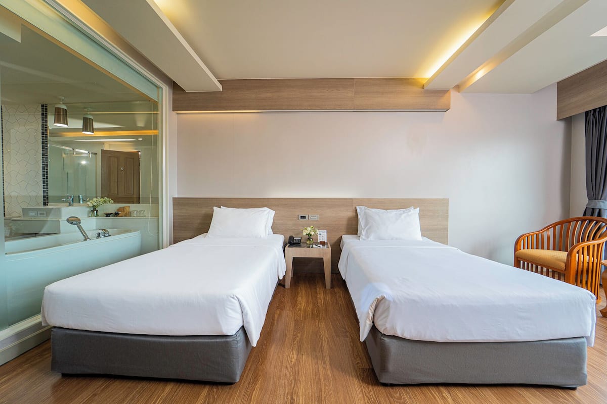 Een hotelkamer met twee bedden, een houten hoofdbord, een nachtkastje met telefoon en vaas, een stoel en een grote spiegel.