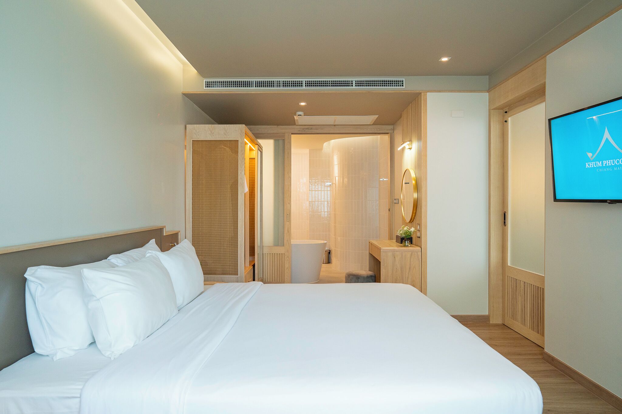 A modern hotel room with a large bed, a bathroom with a shower, and a television on the wall.