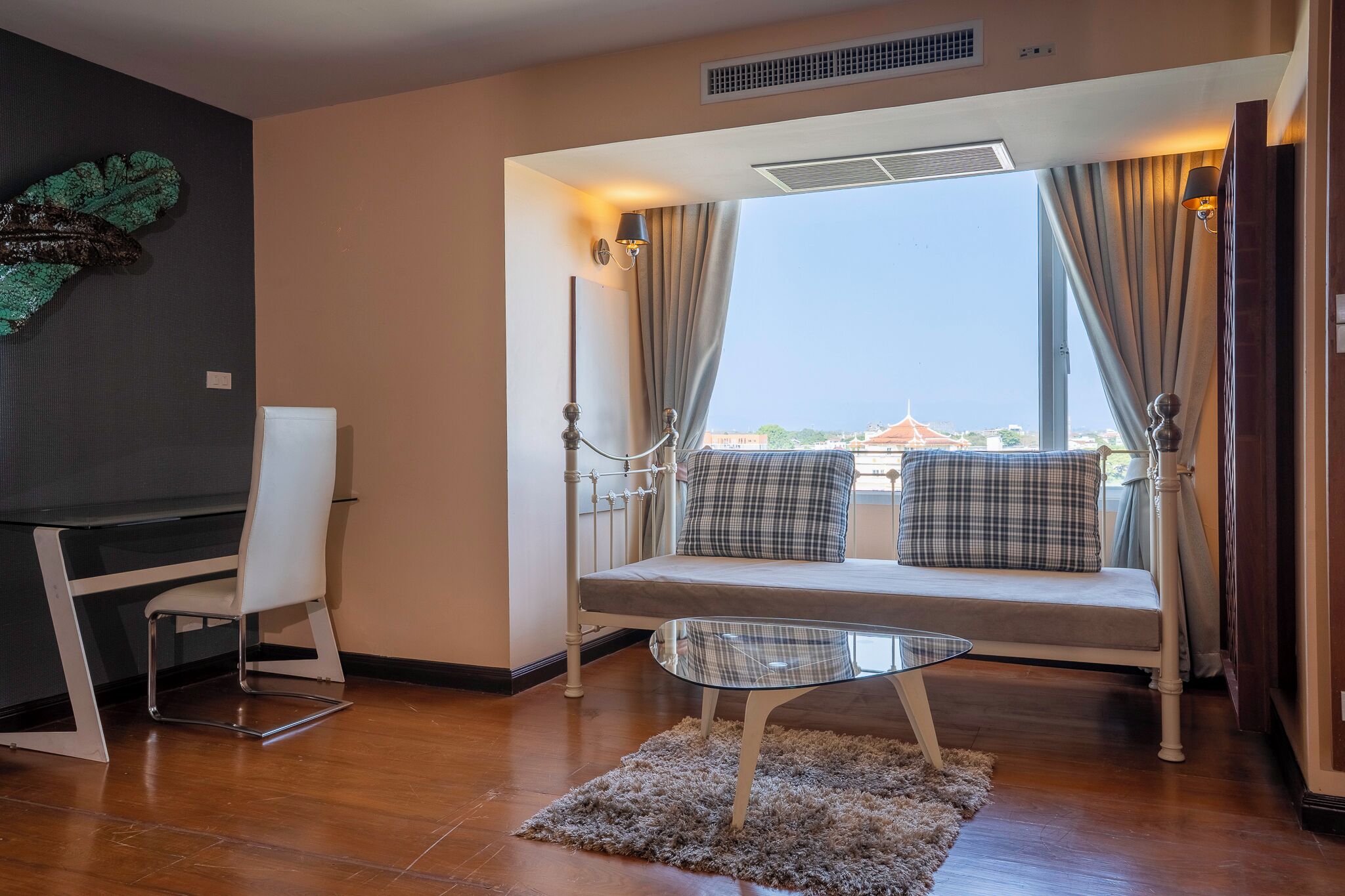 Une pièce moderne comprenant un canapé, une table en verre, une chaise et une vue sur un immeuble à travers de grandes fenêtres.