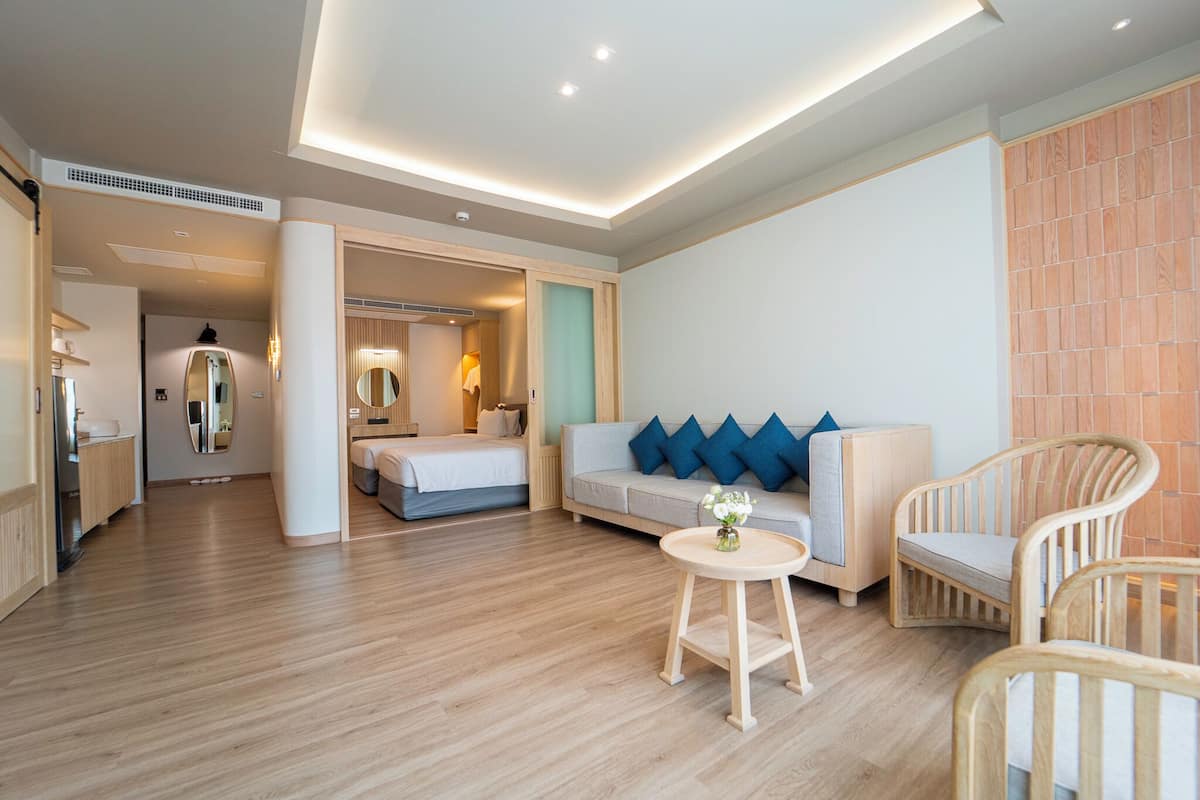 Een moderne hotelkamer met een houten vloer, een bed, een bank met blauwe kussens en twee rieten stoelen.