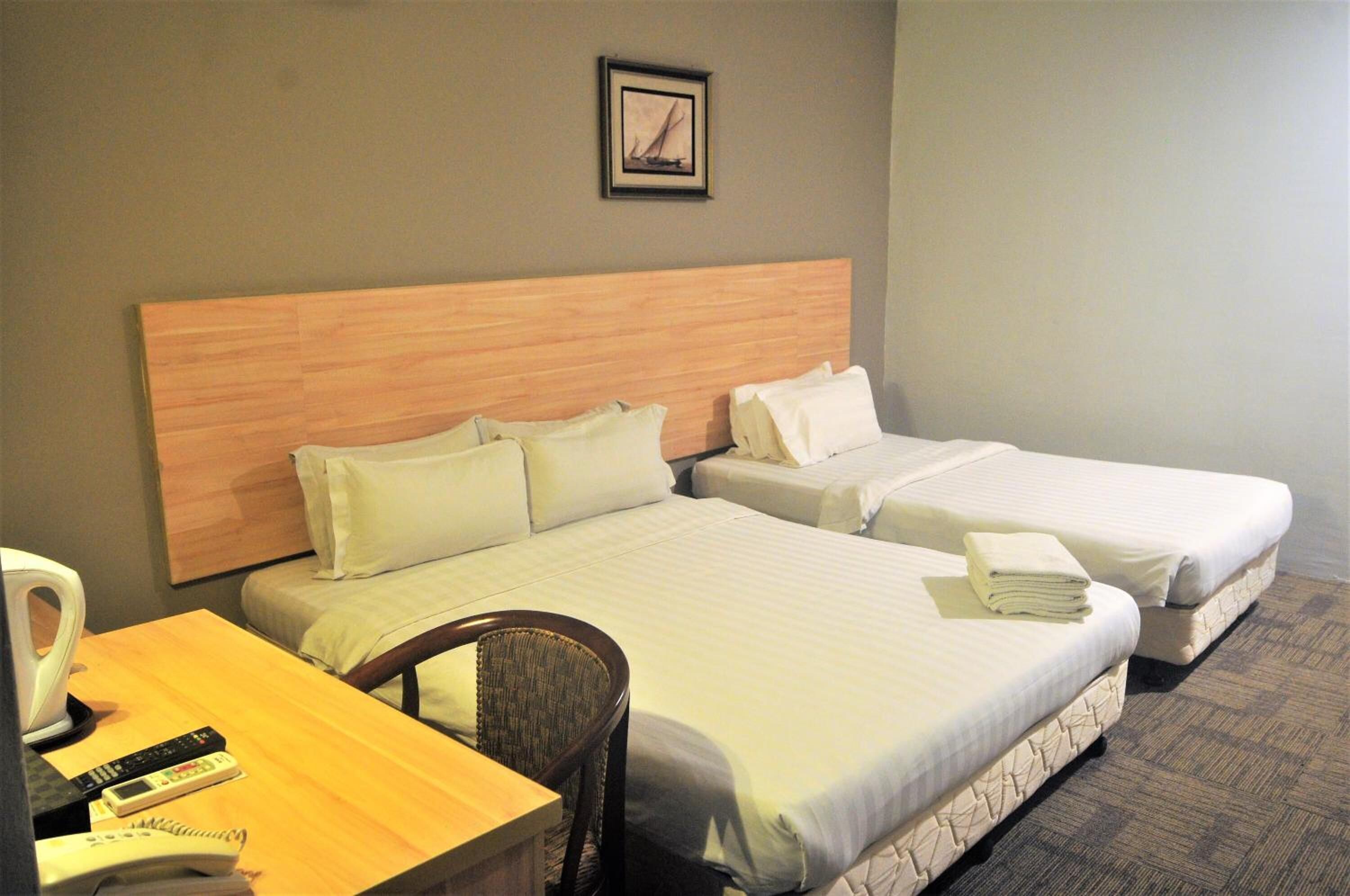 A hotel room with two beds, a wooden headboard, a desk with a chair, a telephone, and a framed picture on the wall.