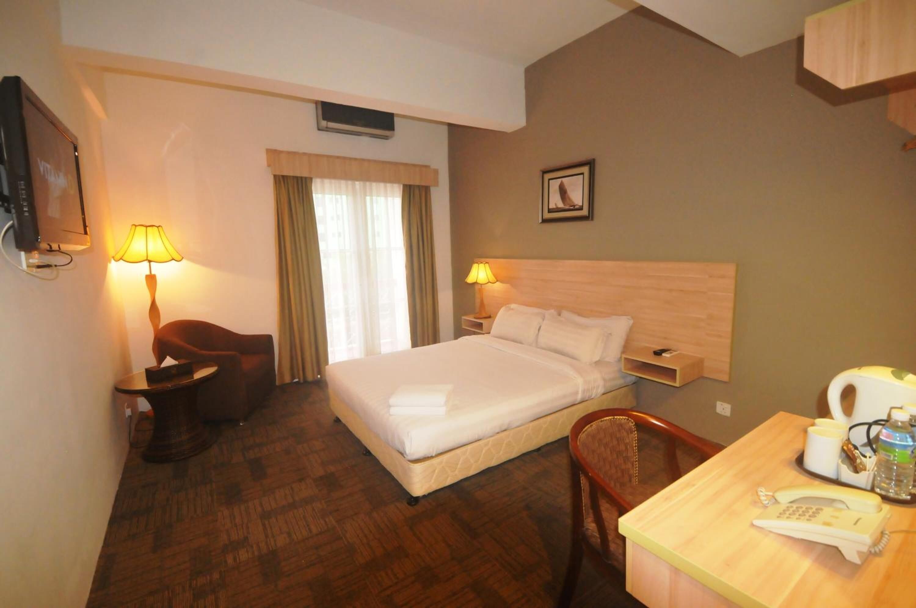 A hotel room with a bed, a desk with a telephone, a chair, a lamp, and a television.