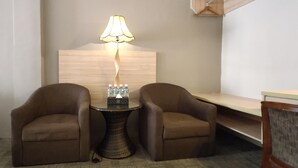 Une chambre d’hôtel avec deux fauteuils marron, une petite table ronde avec une lampe et une tête de lit en bois.