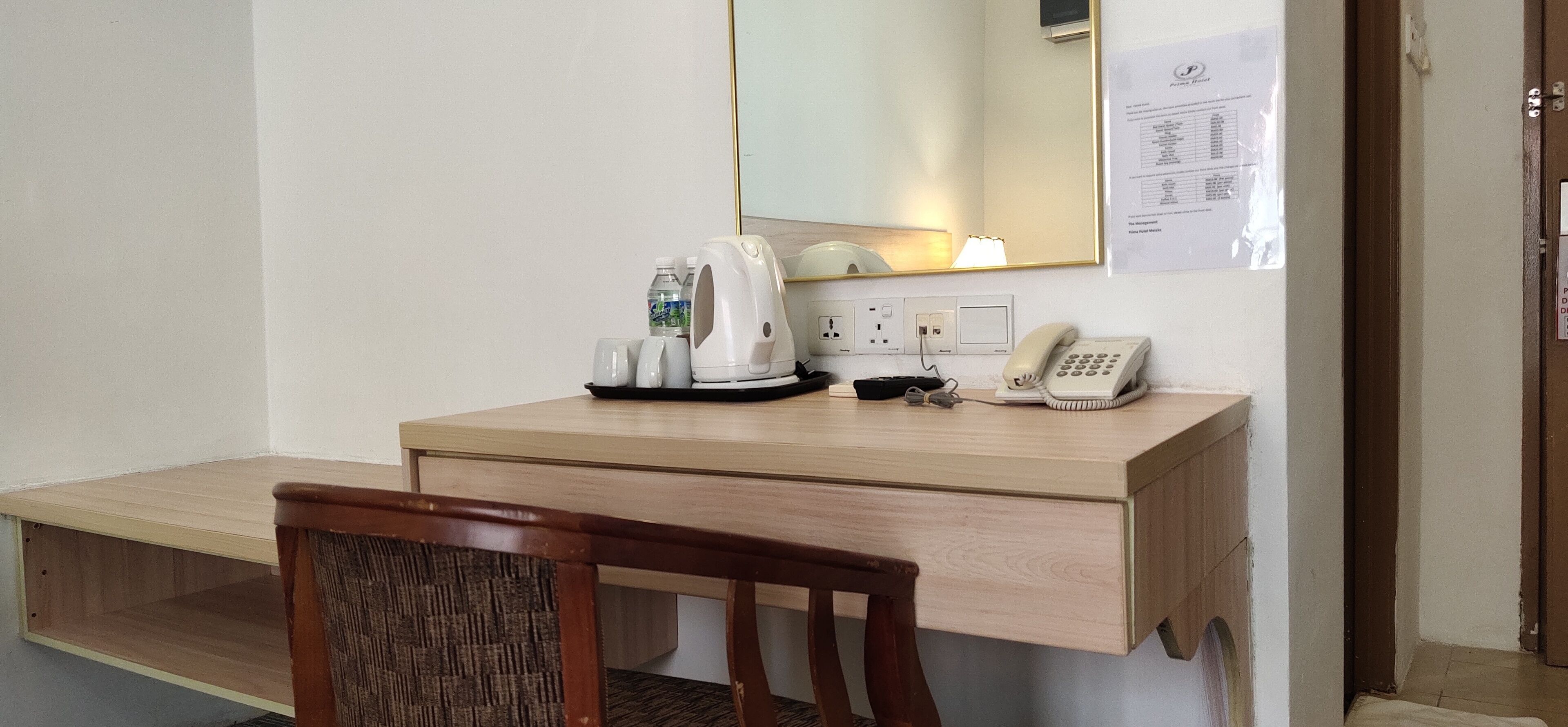A hotel room with a wooden desk, a chair, a coffee maker, a telephone, and a mirror.