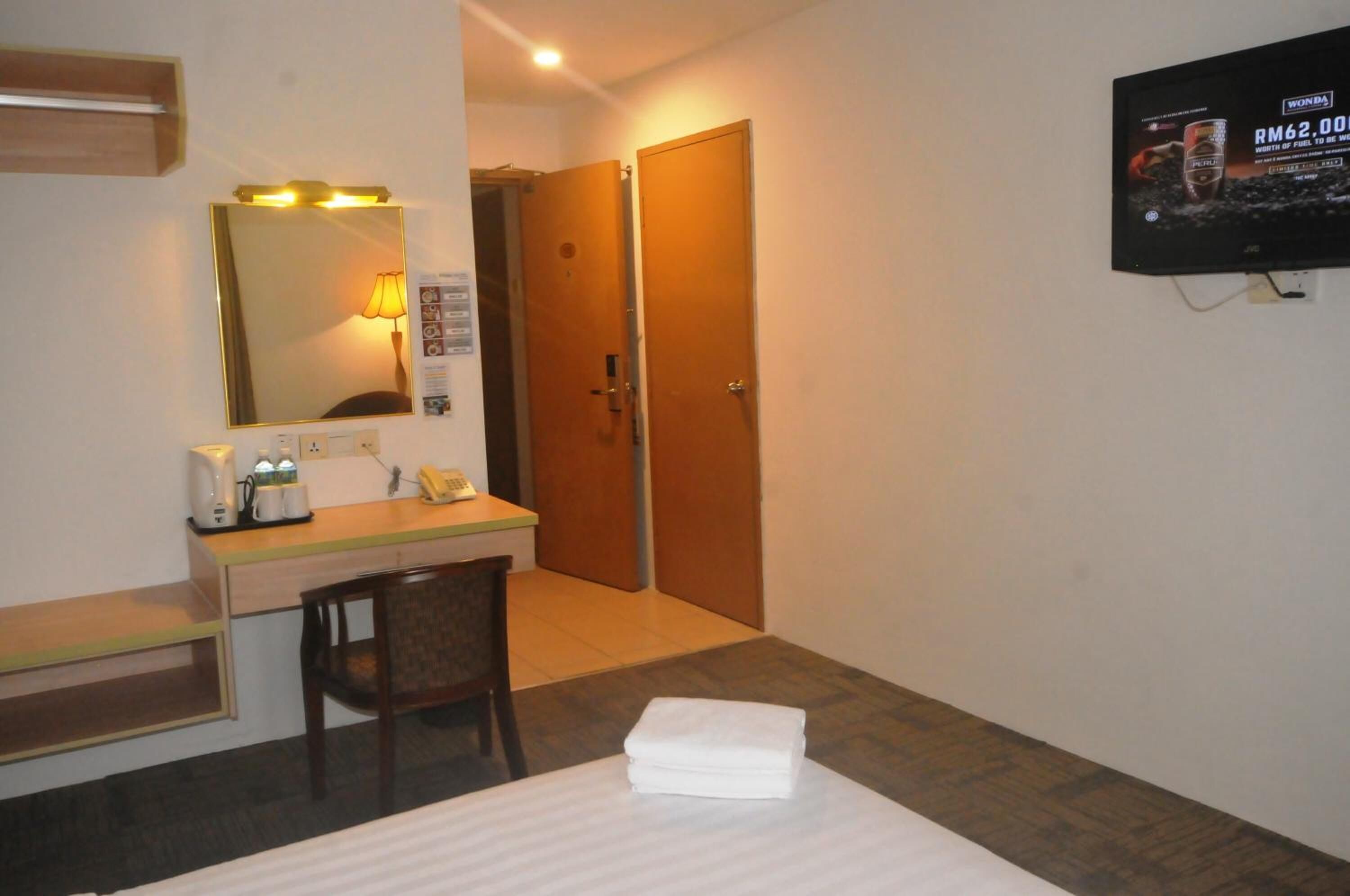 A hotel room with a bed, a desk with a telephone and a lamp, a mirror, and a television on the wall.