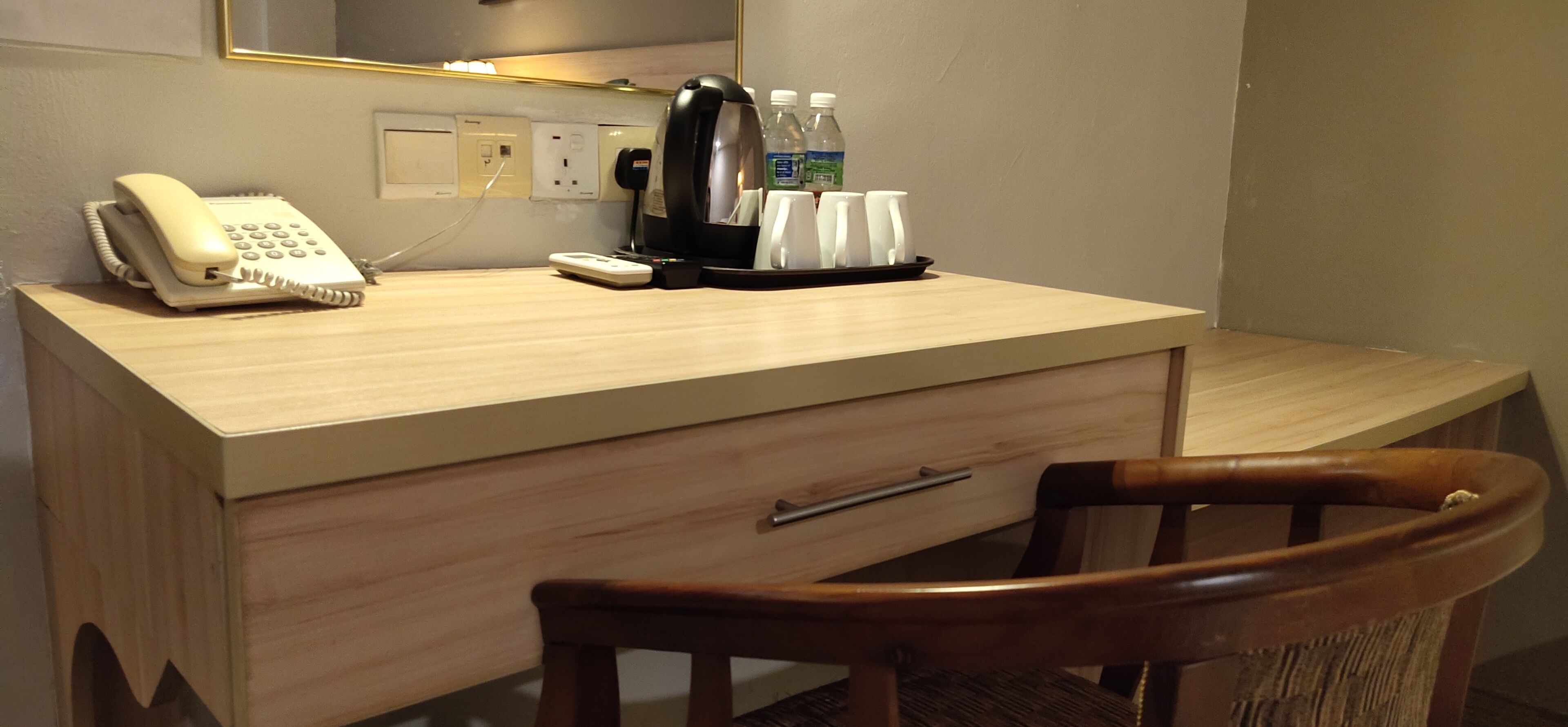 Ein Hotelzimmer mit einem Holztisch, einem Telefon, einer Kaffeemaschine und einem Stuhl.