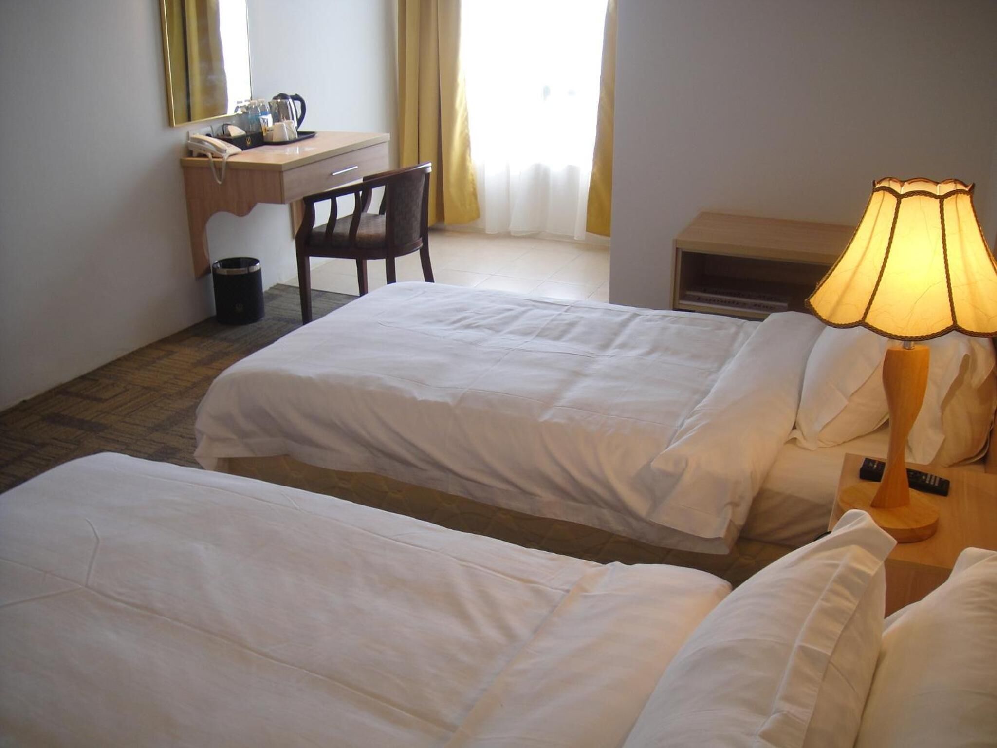 A hotel room with two beds, a desk, a chair, a lamp, and a trash bin.