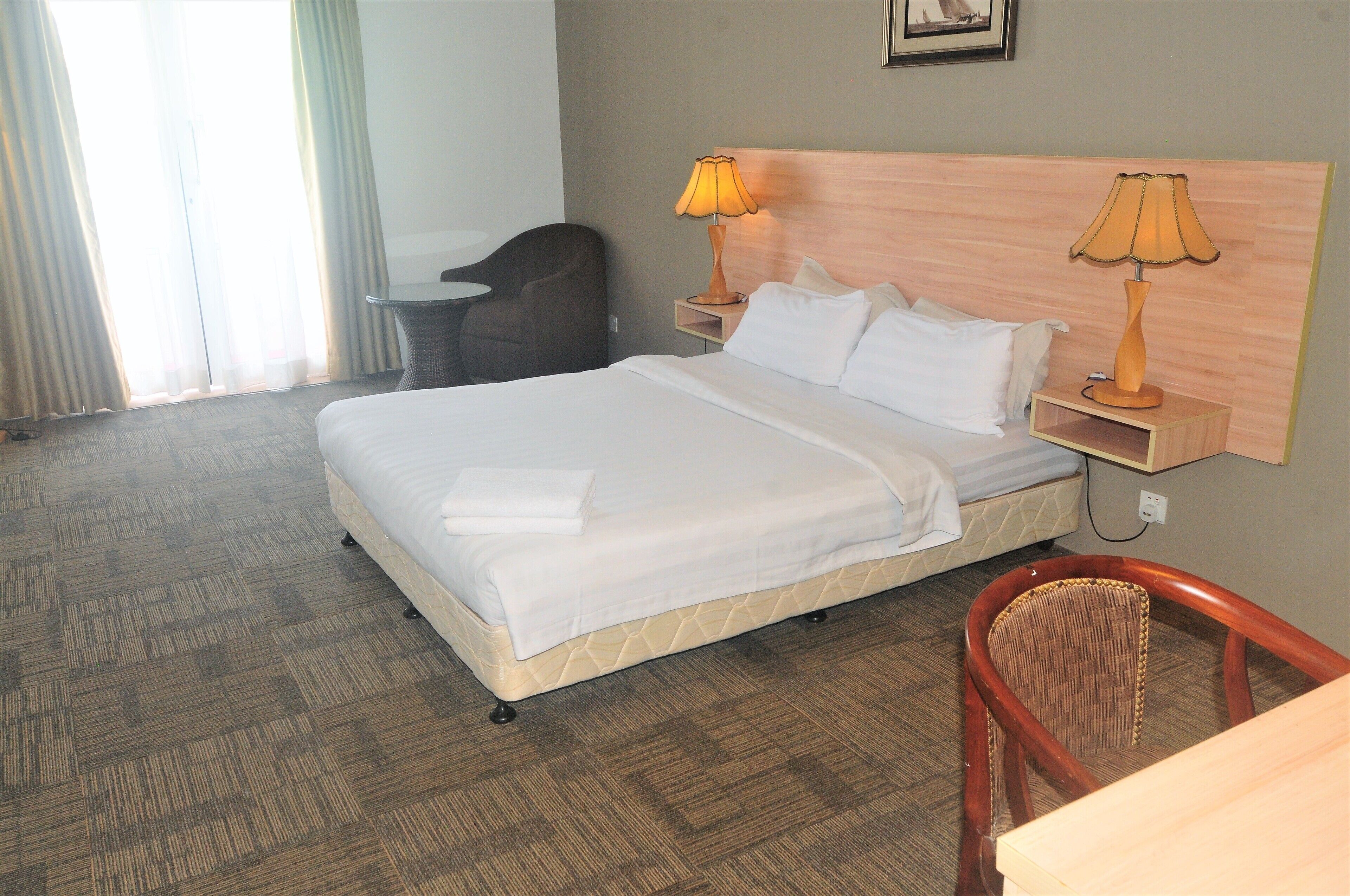 A hotel room with a bed, two bedside lamps, a chair, and a desk.
