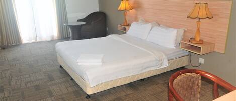 A hotel room with a bed, two bedside lamps, a chair, and a desk.