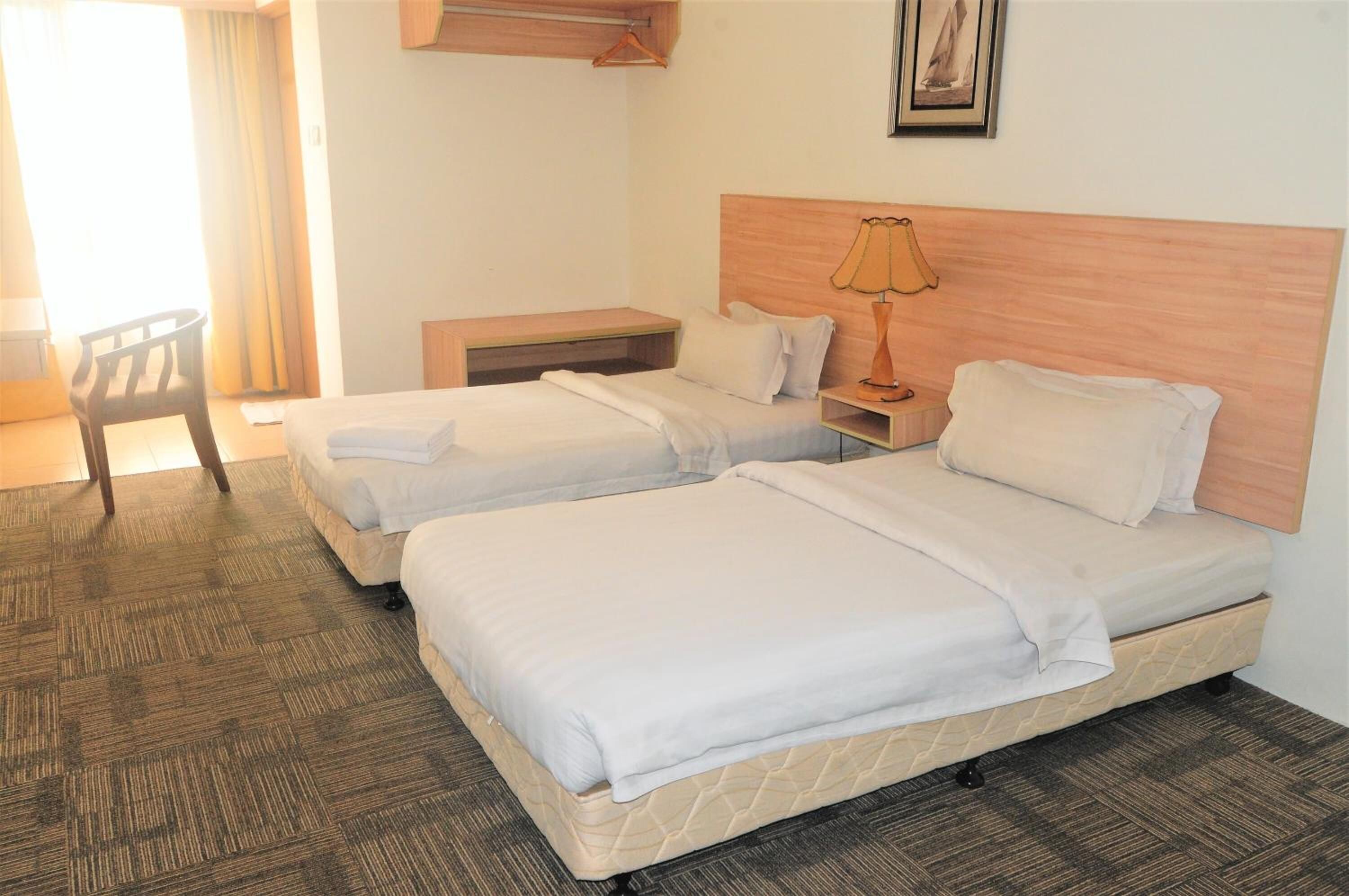 A hotel room with two beds, a small desk, a chair, and a lamp.