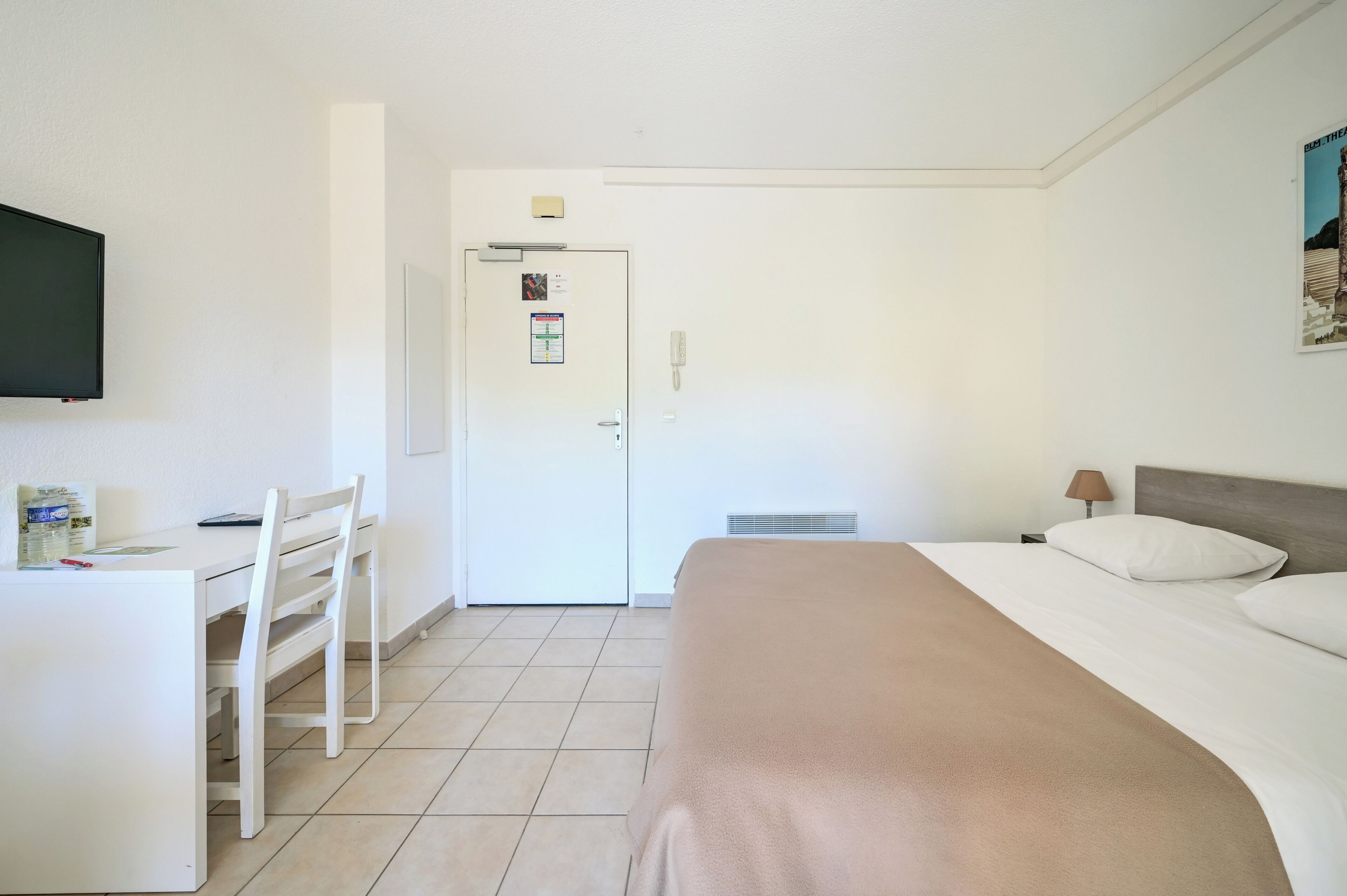 Habitació d'hotel amb un llit, escriptori amb cadira, televisió i una porta amb un avís.