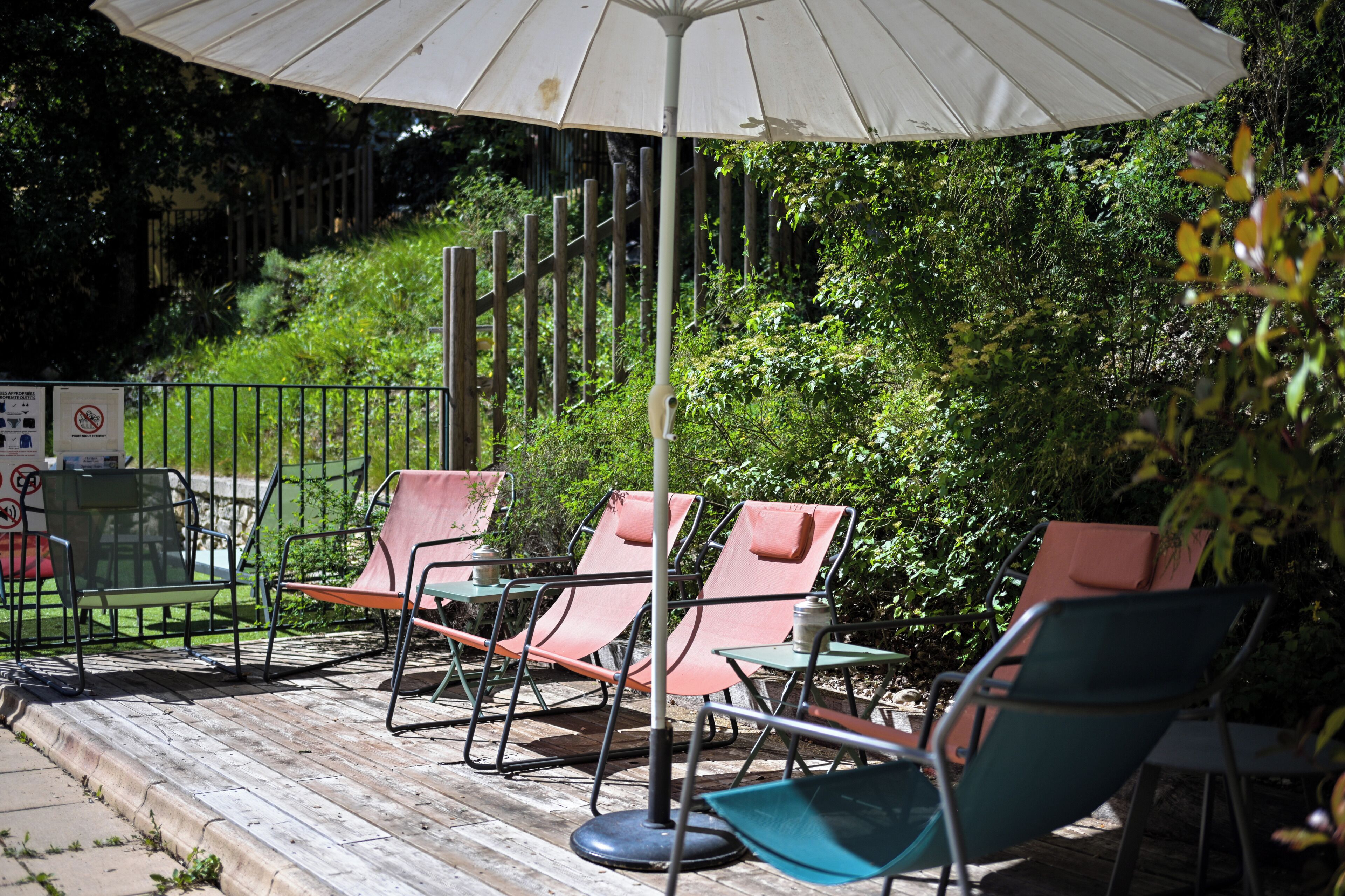 An outdoor seating area with metal chairs and tables, a white umbrella, and a wooden deck.