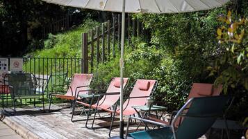 Een terras met metalen stoelen en tafels, een witte parasol en een houten terras.