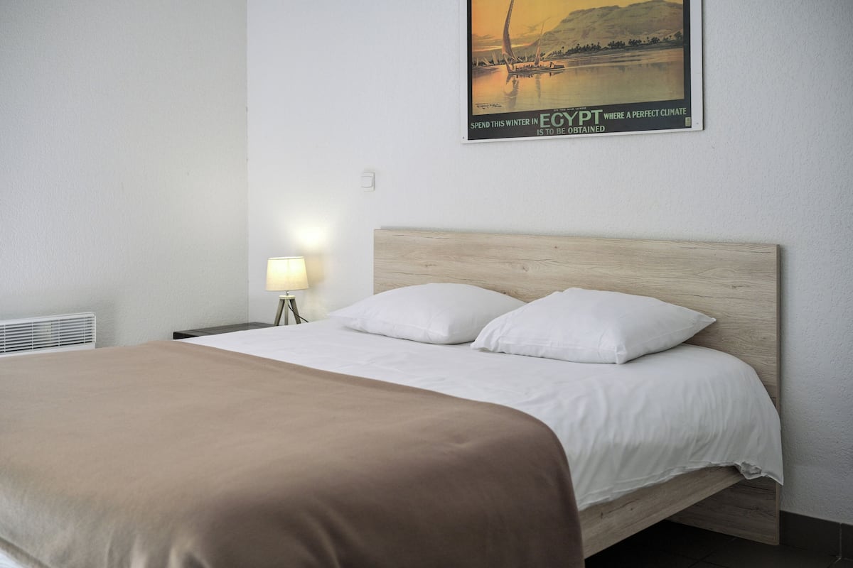 A hotel room with a bed, a nightstand, a lamp, and a poster on the wall.