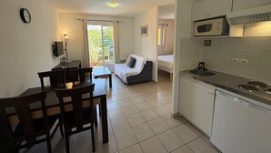 A compact apartment with a kitchenette, a dining area, a sofa, and a balcony with a view.