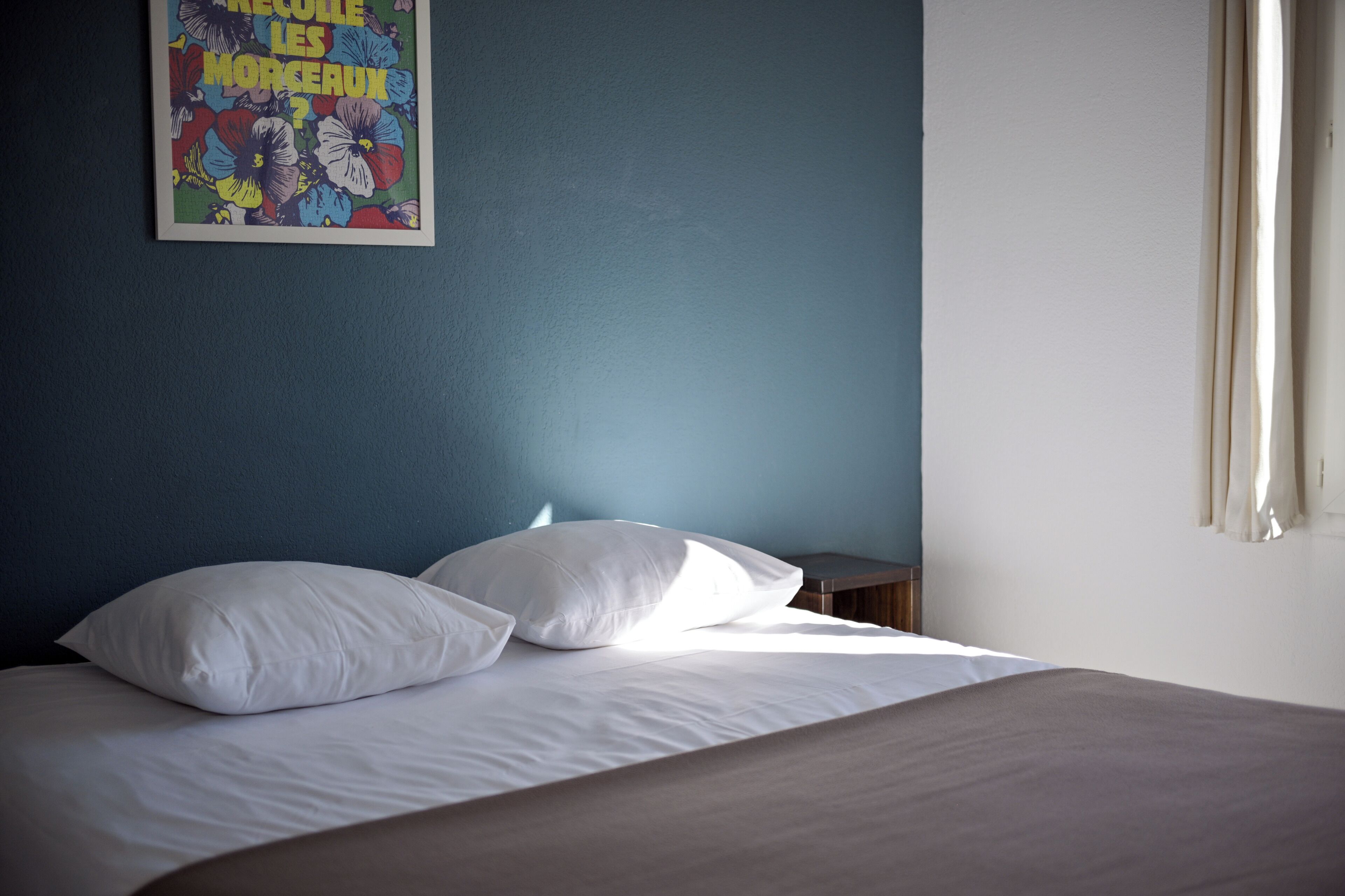 Una cama con ropa blanca, un almohadón y un cartel en una pared azul.