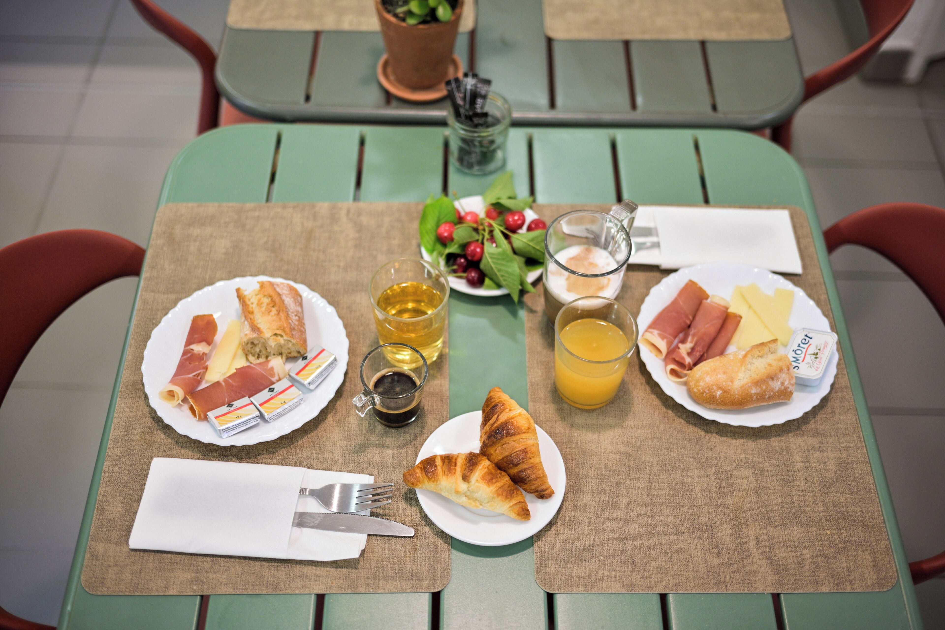 Ein Tisch ist gedeckt mit Frühstücksleckereien wie Croissants, Käse und Obst, dazu ein Glas Saft und eine Tasse Kaffee.
