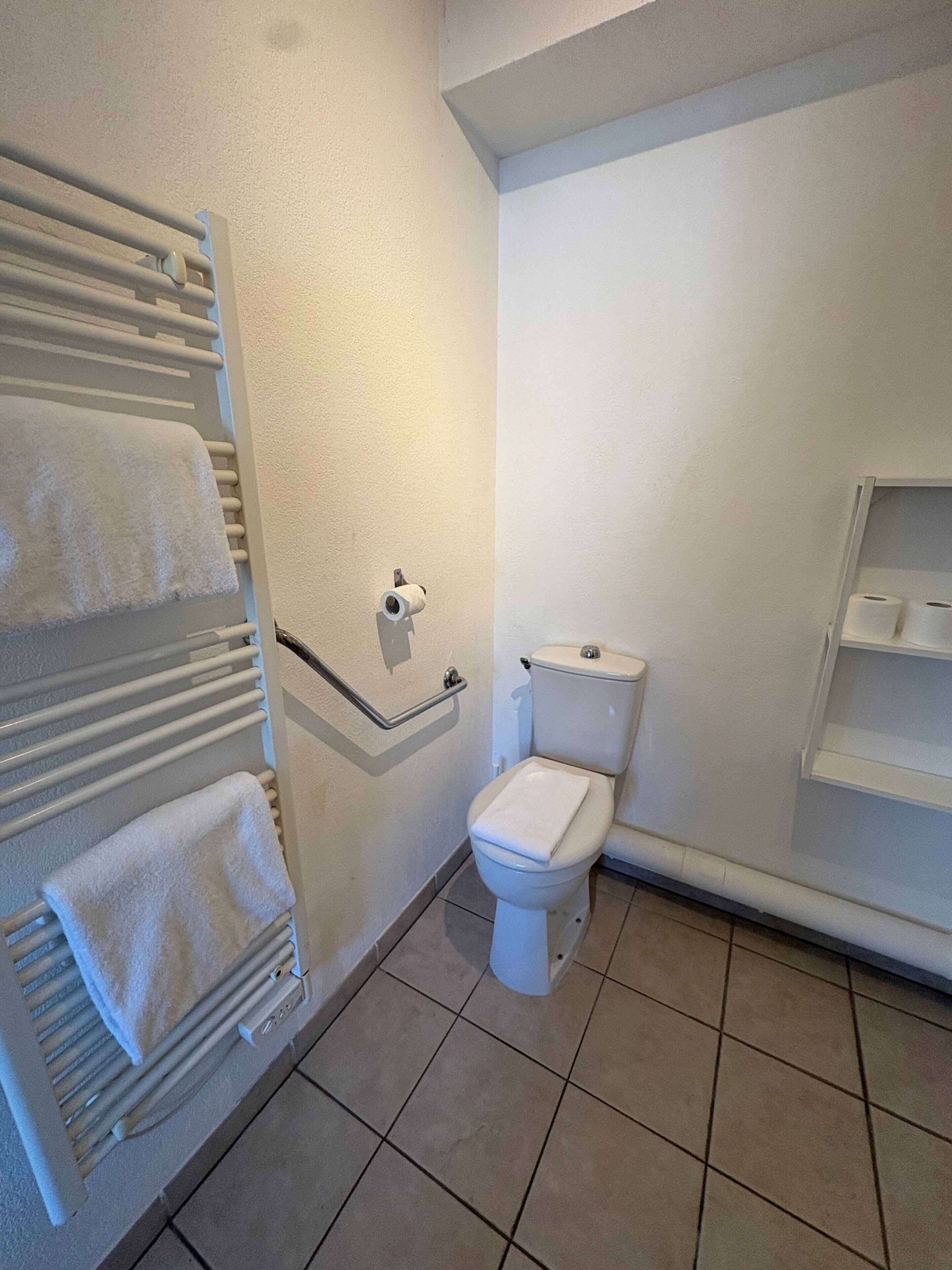Une salle de bain équipée de toilettes, d’un porte-serviettes et d’un support à papier toilette.