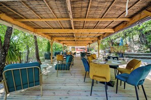 Un espace patio extérieur couvert, doté d’un plancher en bois, de chaises et de tables à ossature métallique.