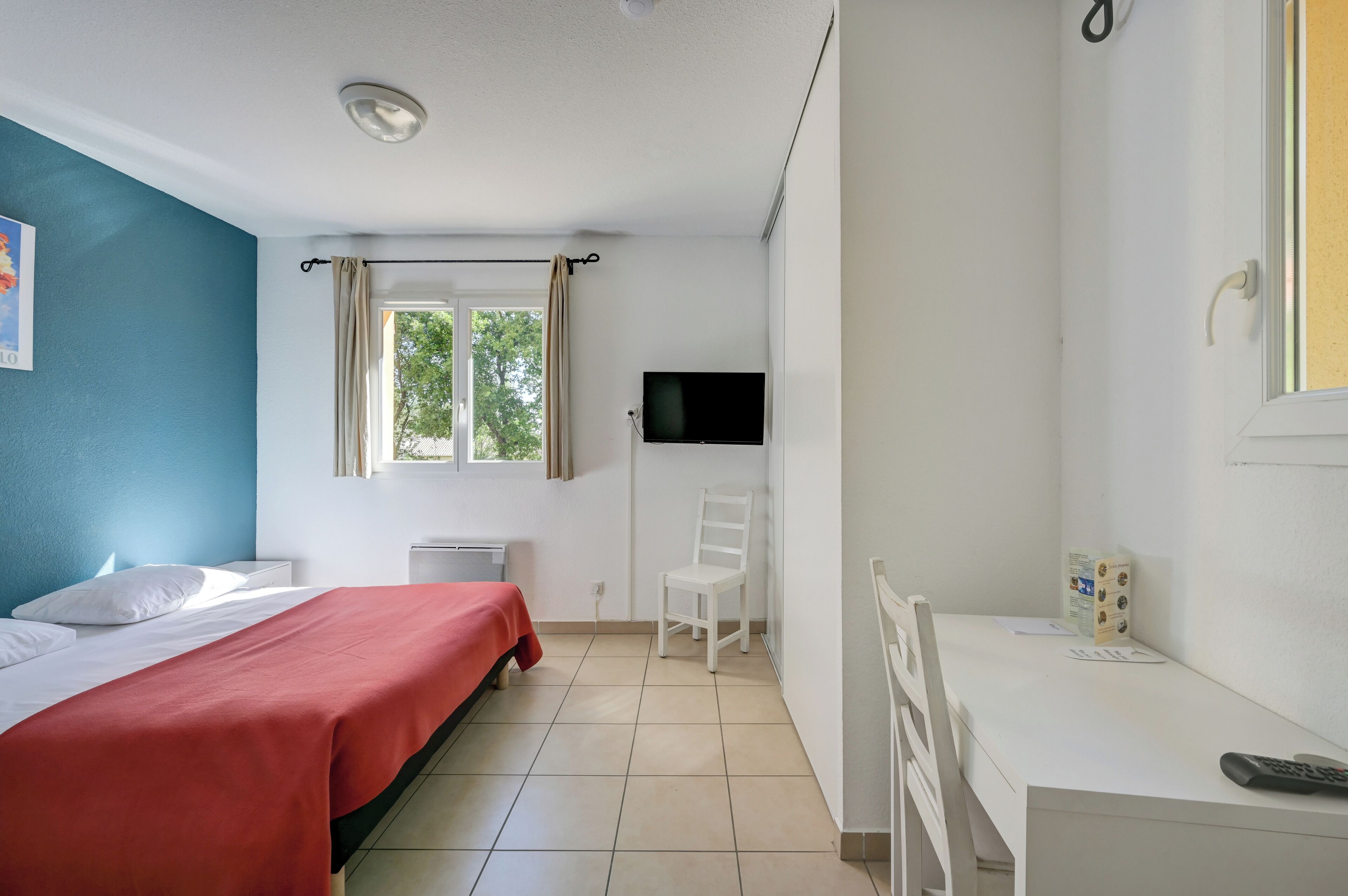 Un dormitorio con cama, escritorio, silla, televisor y ventana.