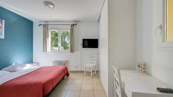 Un dormitorio con cama, escritorio, silla, televisor y ventana.