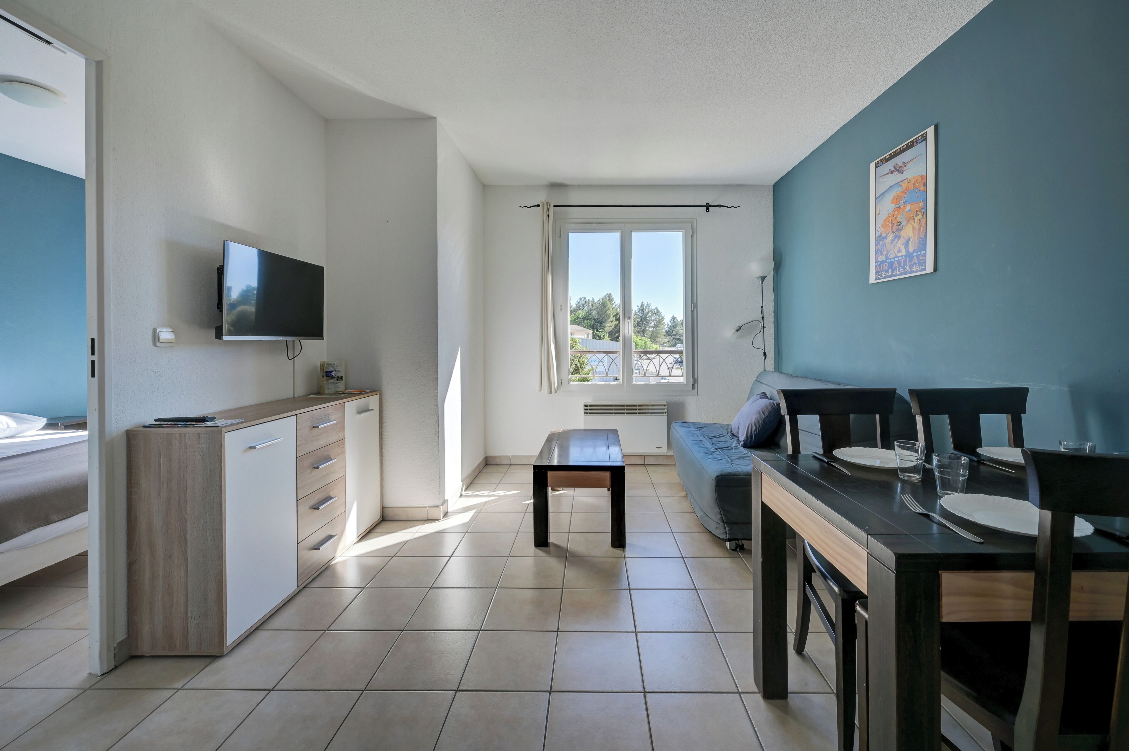 A modern kitchen with a TV, a dining area with a table and chairs, and a sofa.