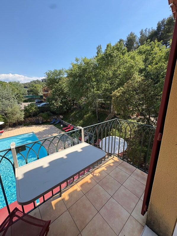 Un balcon avec une piscine, du mobilier d’extérieur et une vue sur une zone boisée.
