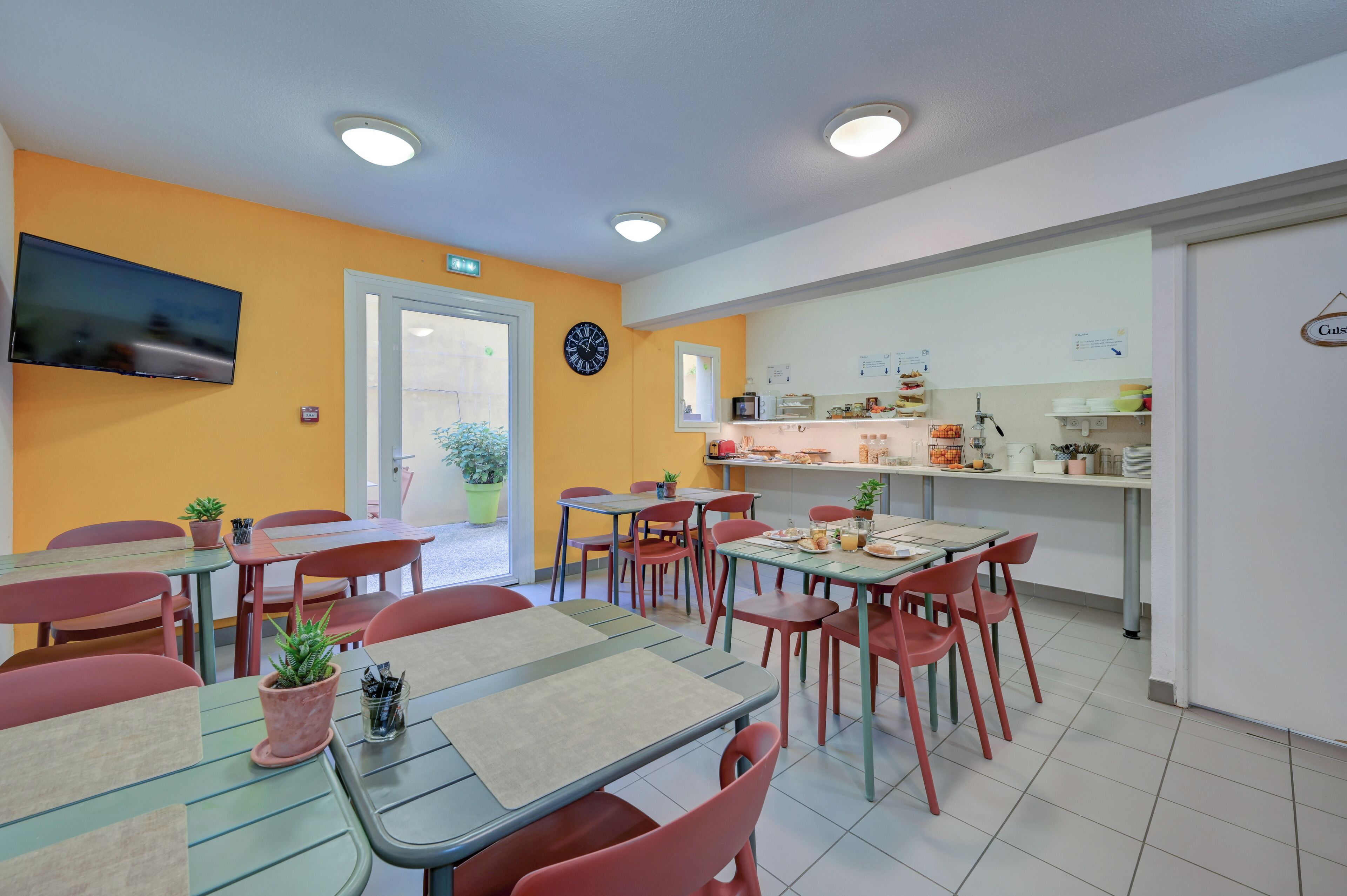 Een eetruimte met tafels, stoelen, een klok en een keuken op de achtergrond.